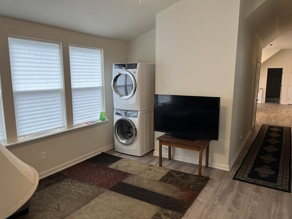 A laundry room with stacked washers and dryers, a flat-screen TV on a stand, and a patterned rug on the floor. - Fishing and Hunting Cottage in Shell Beach, St. Bernard, LA (Saint Bernard)