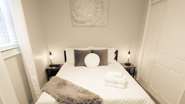 Un dormitorio ordenado con cama, mesitas de noche, una lámpara colgante y una obra de arte en la pared.