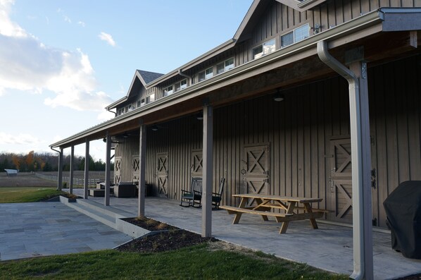 Een overdekt buitengebied met een picknicktafel en banken, een overdekte veranda en een schuurachtig gebouw met grote deuren.