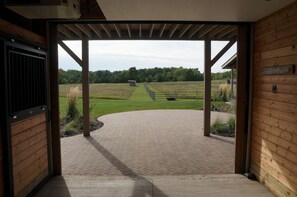 Een open houten constructie met een verharde opgang naar een grasveld.