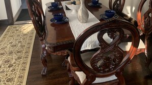 Ein Esszimmer mit Holztisch, Stühlen und einer Vase. Ein Fenster mit Milchglas und eine Tür zu einer Küche sind ebenfalls vorhanden.