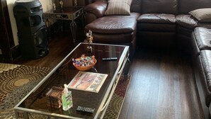Ein Wohnzimmer mit einem braunen Ledersofa, einem Glastisch mit einer Zeitschrift, einer kleinen Pflanze und einem Lautsprecher.