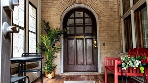 A brick entrance with a dark wooden door, a small table with chairs, and a potted plant. - MKE Mansion - East Wing Private Home (Milwaukee)