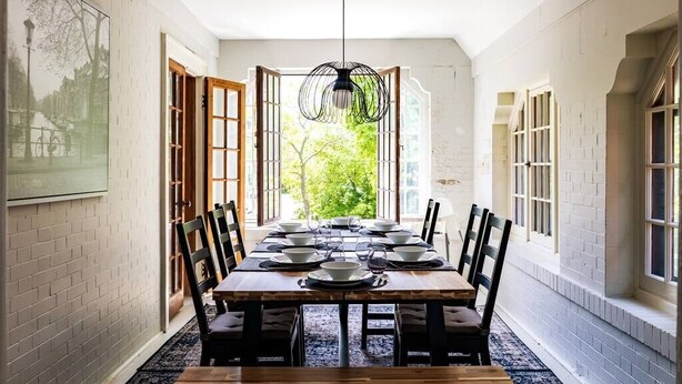 A dining area with a long wooden table set for six, surrounded by chairs, with a hanging light fixture above. - MKE Mansion - East Wing Private Home (Milwaukee)
