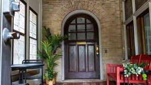 A wooden-floored porch with a bench, a potted plant, and a door with a glass panel. - MKE Mansion - East Wing Private Home (Milwaukee)