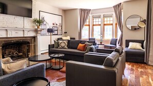A modern living room with a fireplace, a large sofa set, a coffee table, and a TV mounted on the wall. - MKE Mansion - East Wing Private Home (Milwaukee)