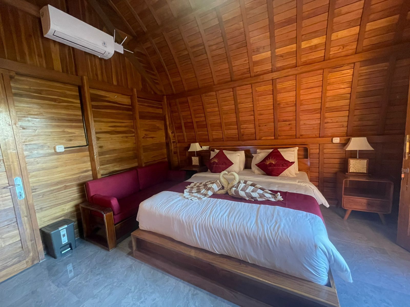 A wooden cabin-style room with a bed, a red sofa, and a small table.