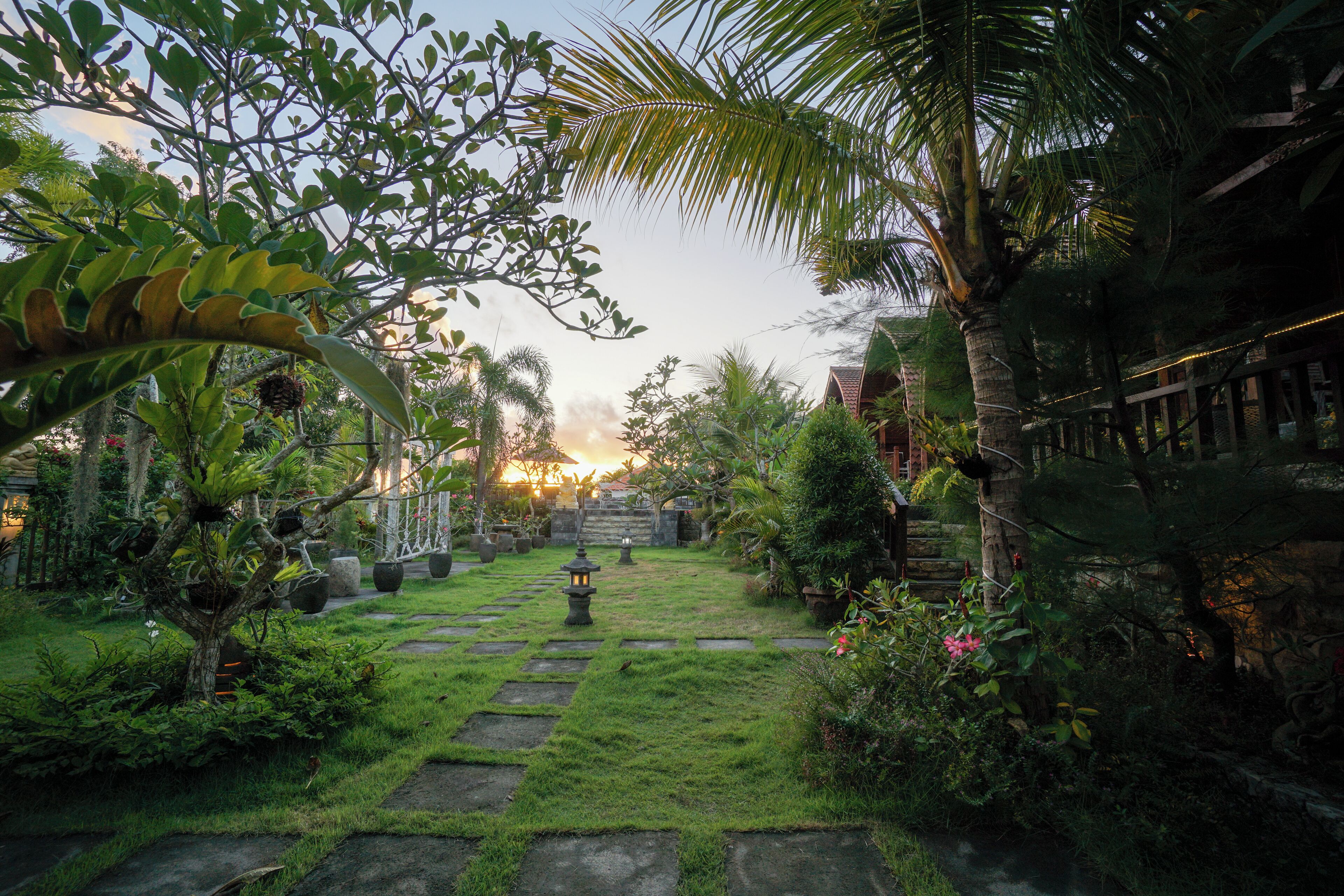 A garden pathway with stepping stones, surrounded by lush greenery and a stone wall.