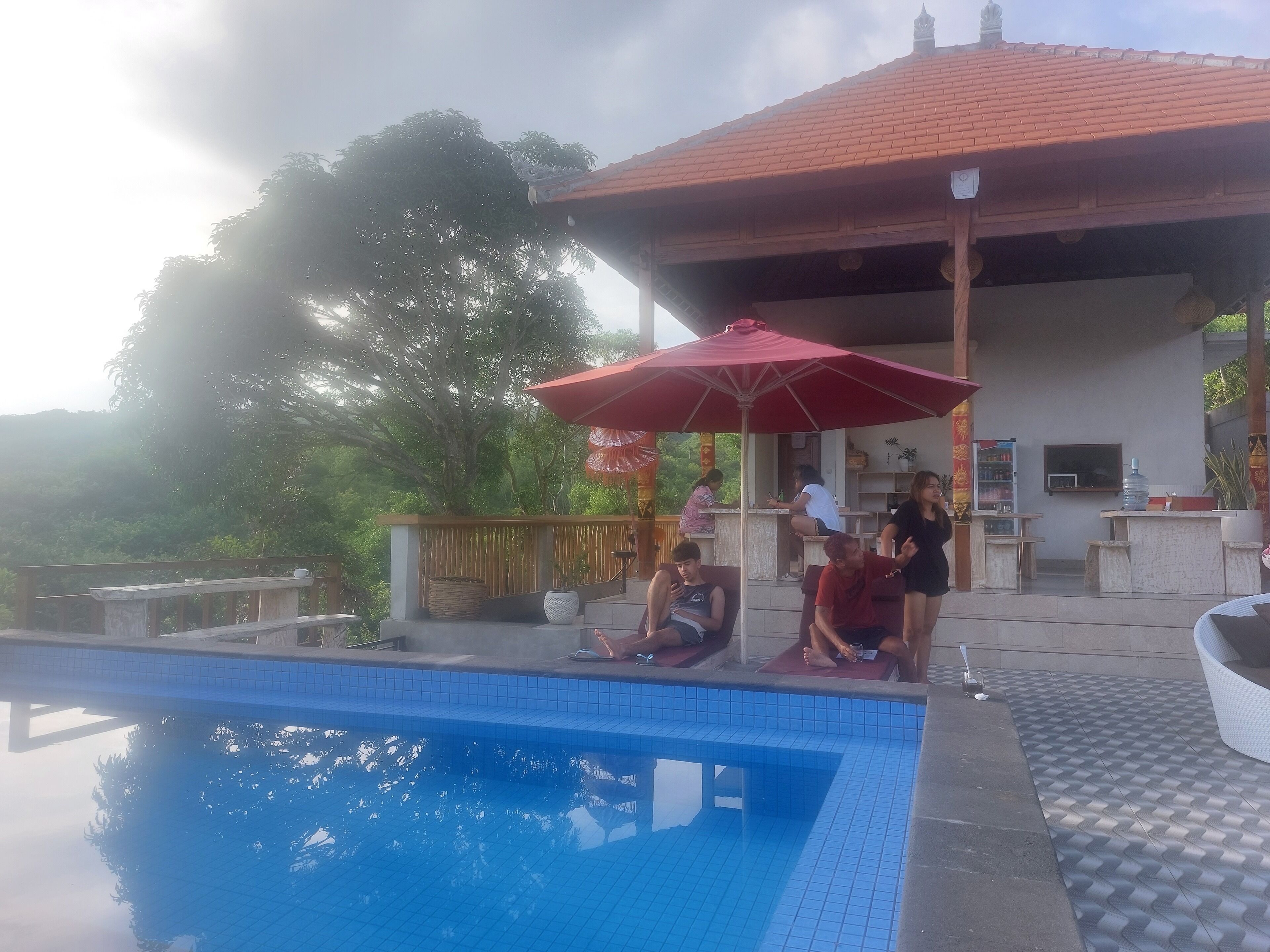 A swimming pool area with a covered seating area, a water dispenser, and a bar.