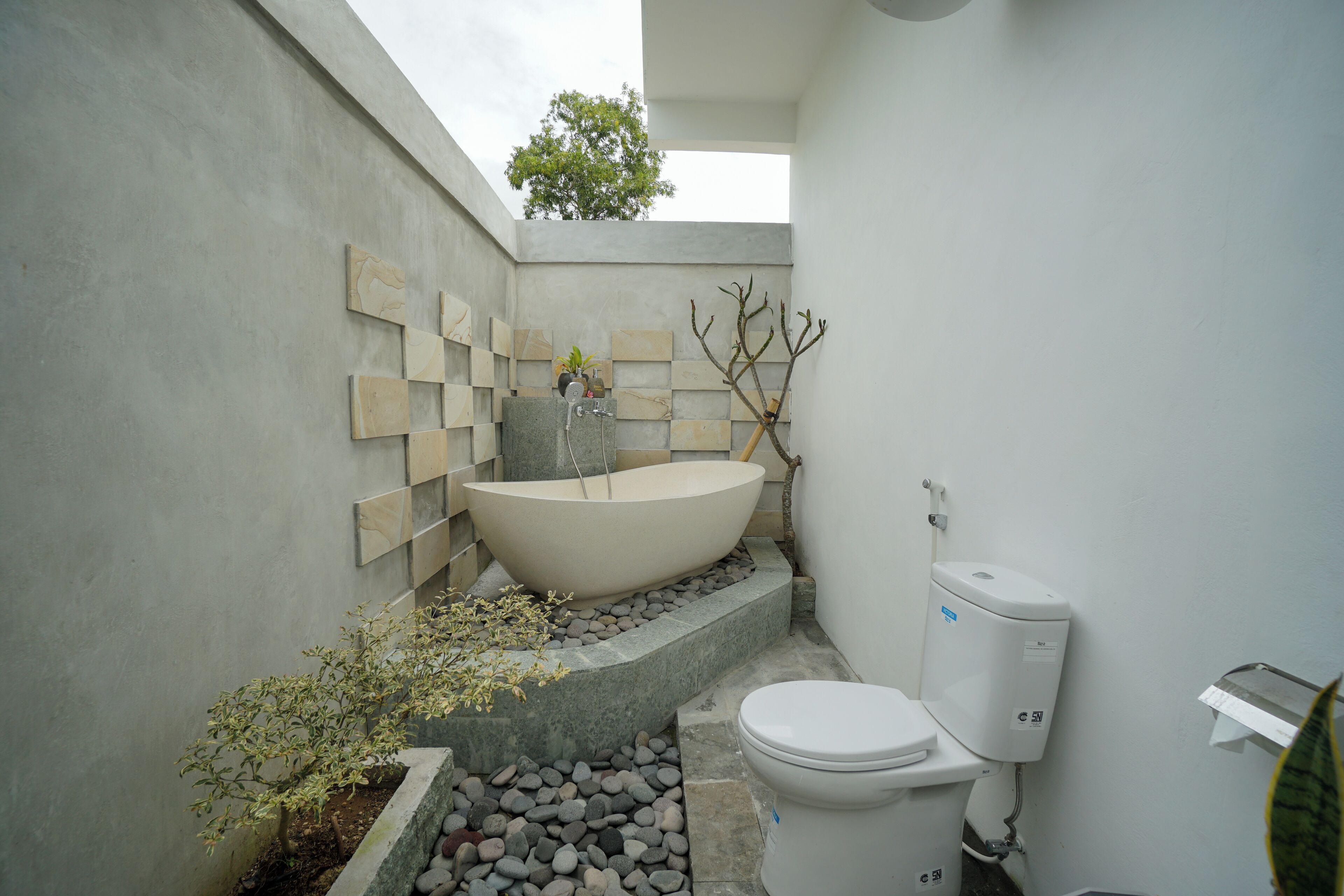 A modern bathroom with a freestanding bathtub, a toilet, and a small plant area.