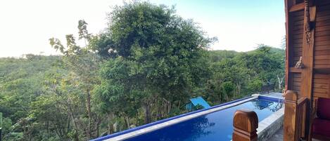 A pool with a wooden deck and a view of a forested area.
