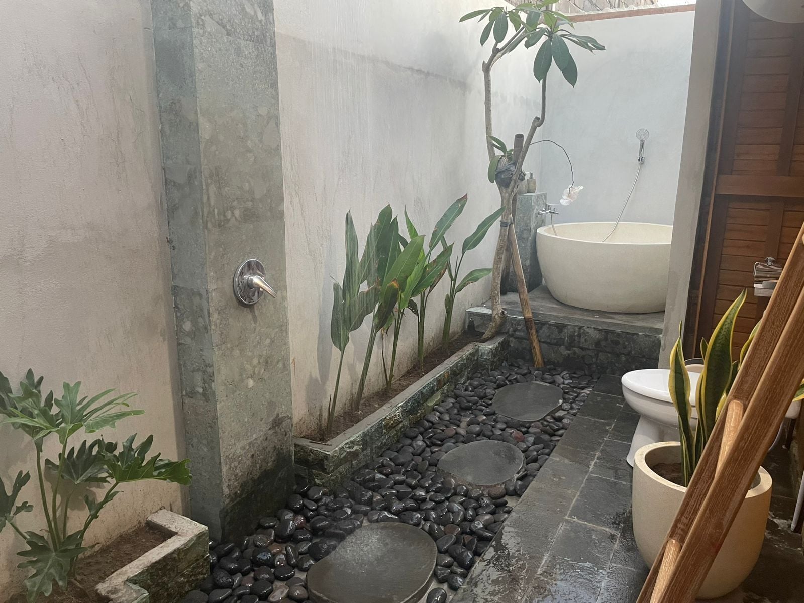A bathroom with a bathtub, a toilet, and a sink. There are plants and a small garden area with rocks.