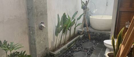 A bathroom with a bathtub, a toilet, and a sink. There are plants and a small garden area with rocks.
