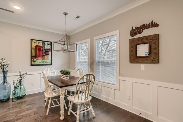 A dining area with a wooden table and white chairs, a chandelier, and decorative items on the walls.