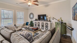Ein Wohnzimmer mit Deckenventilator, Fernseher, einer Vitrine mit Dekoration und einer grünen Kommode mit Lampe.