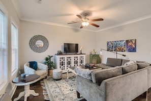A living room with a grey sofa, a small round table, a white cabinet, a ceiling fan, and a TV.