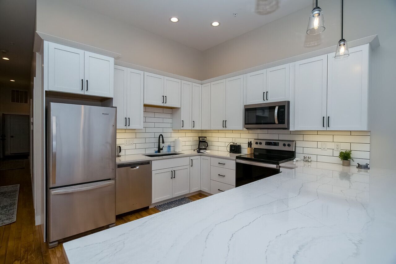 A modern kitchen with white cabinets, stainless steel appliances, and a marble countertop.