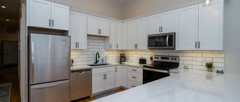 A modern kitchen with white cabinets, stainless steel appliances, and a marble countertop.