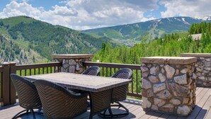 Eine Holzterrasse mit einem Steintisch und Korbstühlen, mit Blick auf eine gebirgige Landschaft.