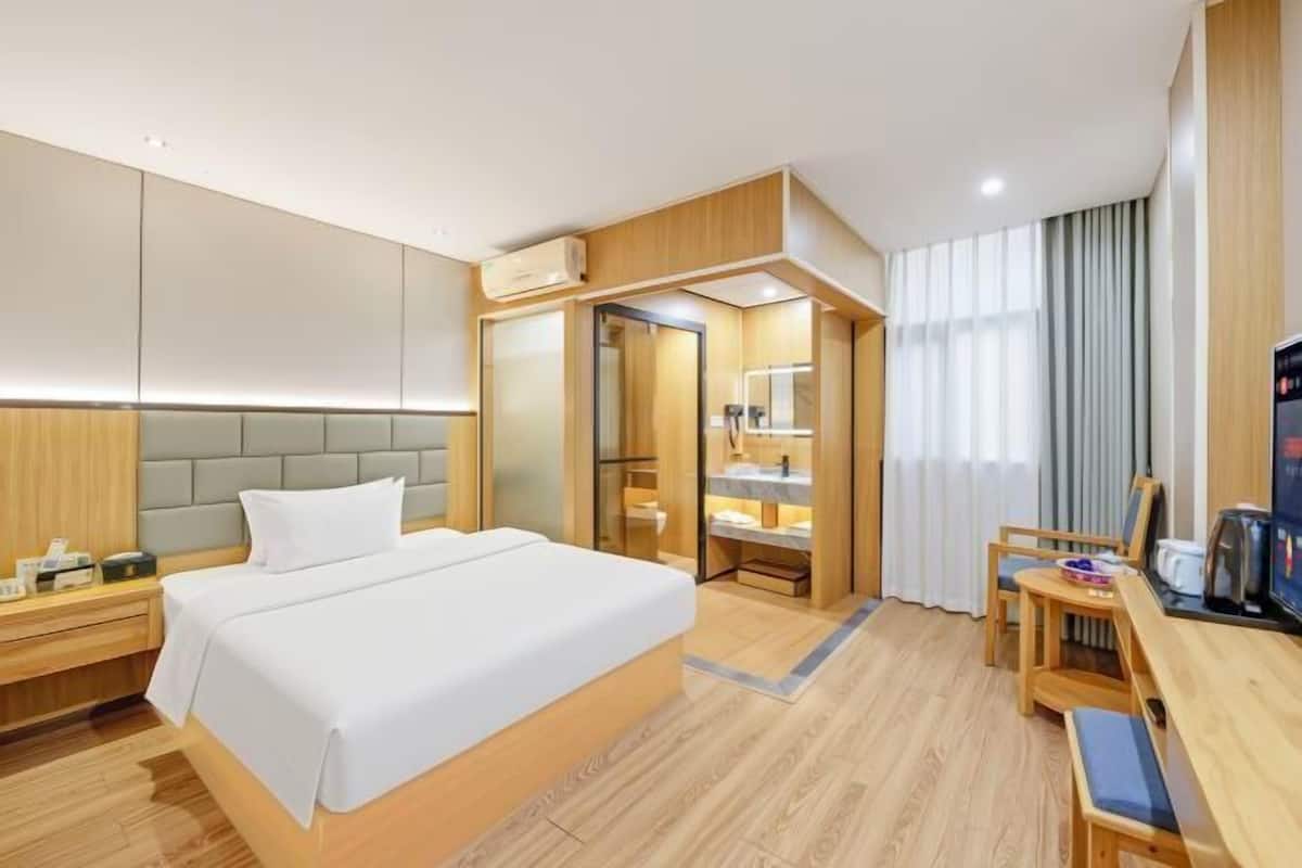 A hotel room with a large bed, a desk with a chair, a TV, and a bathroom with a mirror and sink.