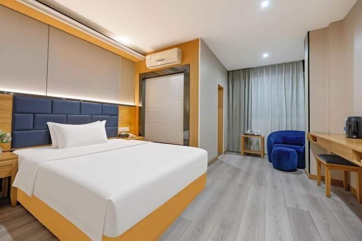 A modern hotel room with a large bed, a desk, a chair, and a wardrobe.