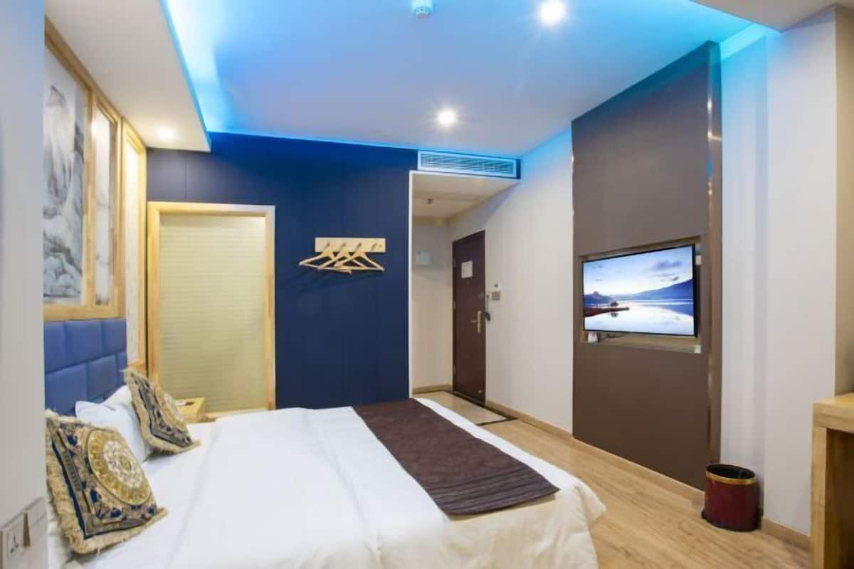 A modern hotel room with a bed, a television, and a blue accent wall.