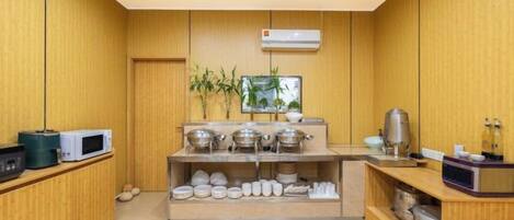 A compact kitchen with wooden paneling, a microwave, a coffee machine, and a shelf with dishes.