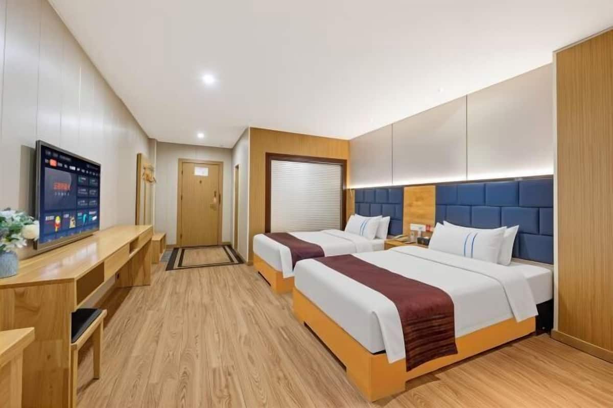 A hotel room with two beds, a desk, and a TV.