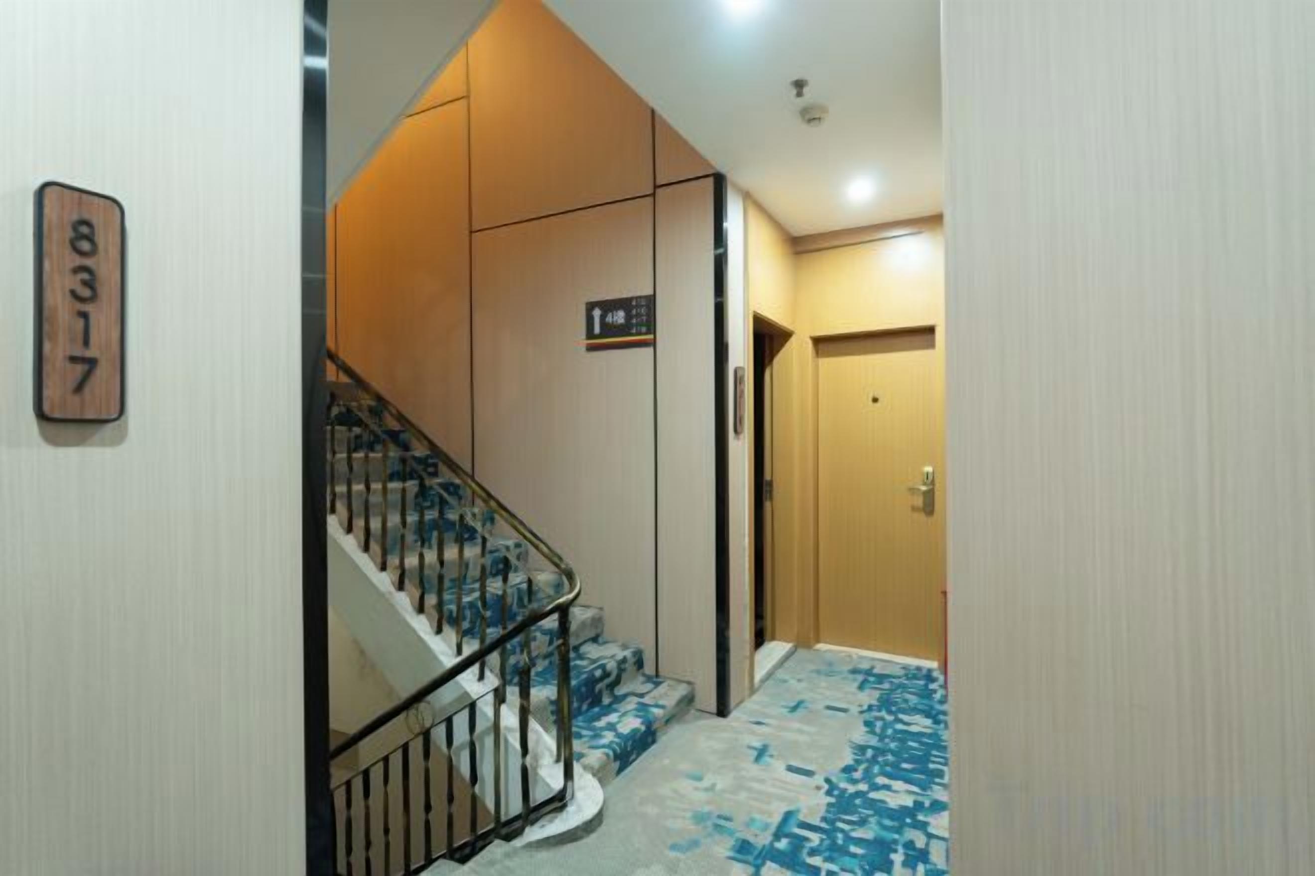 Un pasillo de hotel con una escalera, una puerta de madera y una alfombra con diseño geométrico.