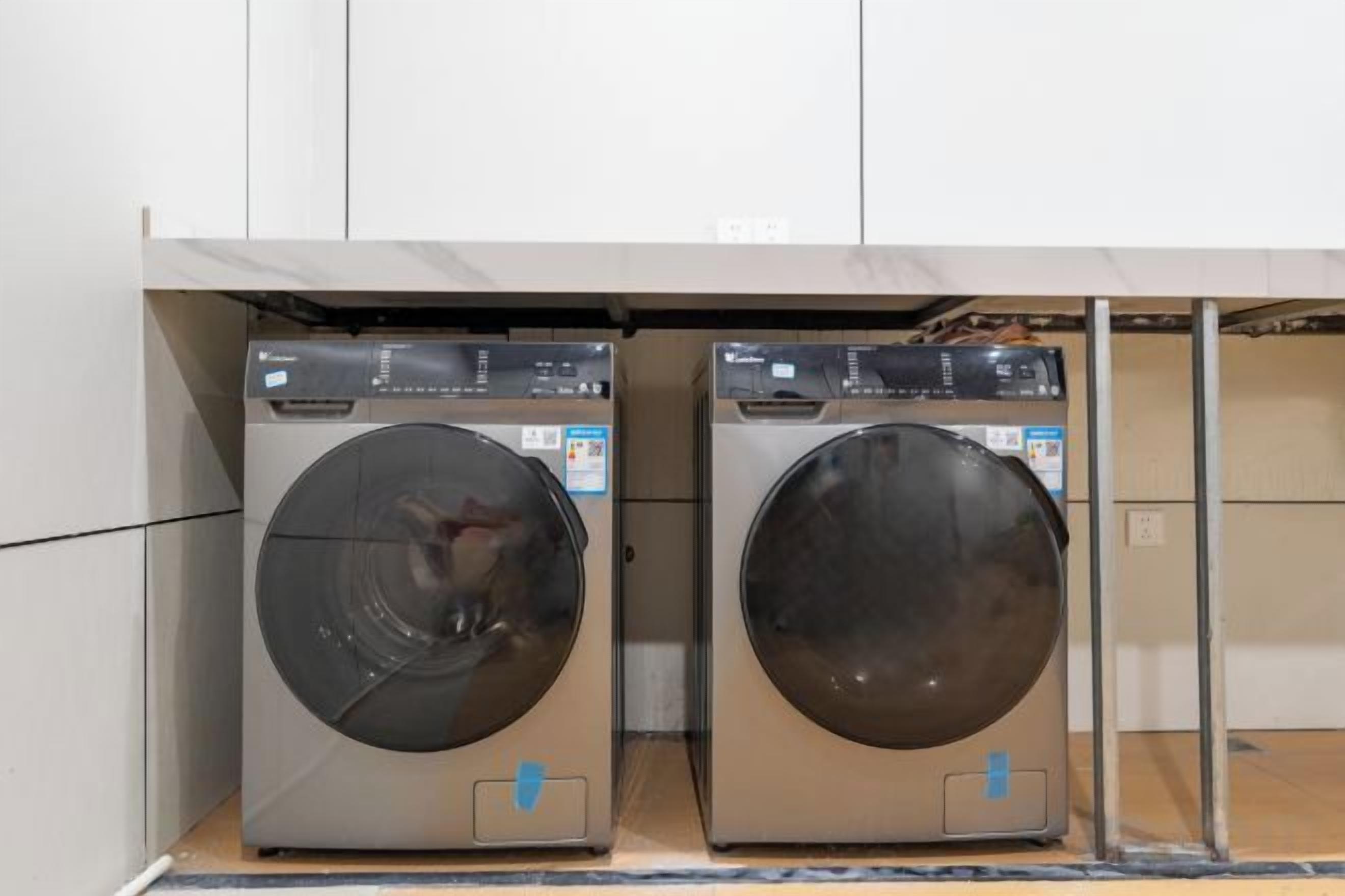 Two front-loading washing machines in a laundry room with a tiled floor and a white wall.