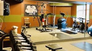 Une salle de sport équipée de matériel d’exercice, d’un banc et d’un téléviseur fixé au mur.