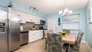 A modern kitchen with white cabinets, stainless steel appliances, and a dining area with patterned chairs and a wooden table. - ⭐BEACHSIDE BLISS!⭐Singer Island 2/2⭐Huge Pool+Spa (West Palm Beach)