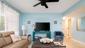 A living room with a beige sofa, a coffee table, a teal entertainment unit, and a television. - ⭐BEACHSIDE BLISS!⭐Singer Island 2/2⭐Huge Pool+Spa (West Palm Beach)