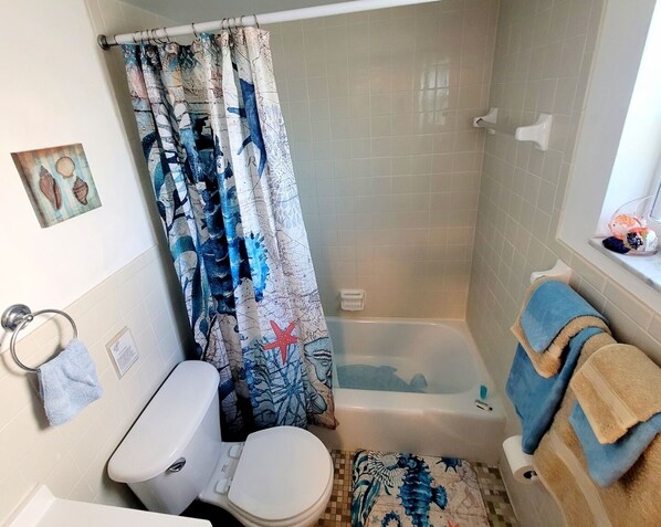 Un baño con bañera, inodoro y cortina de ducha con temática náutica.