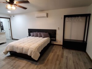A bedroom with a bed, a ceiling fan, an air conditioner, and a door with a curtain.