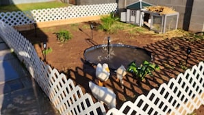 A backyard with a fenced play area, a small pond, and a bird feeder.