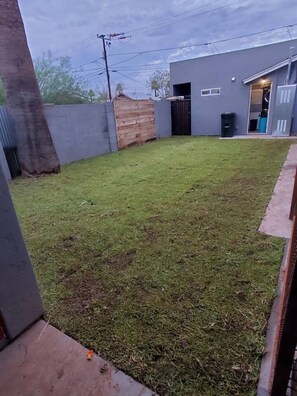 A backyard with a grassy lawn, a wooden fence, and a grey building with an open door.