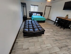 A compact room with a bed, a sofa, a desk, and a TV.