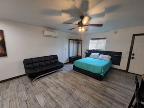 A bedroom with a bed, a black sofa, a ceiling fan, and a wooden floor.