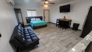 A compact room with a bed, a sofa, a small dining table, and a TV mounted on the wall.