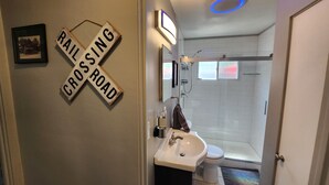 A bathroom with a sink, toilet, and shower. There is a 'Rail Crossing' sign on the wall. - The Railroad Ranch - Station Five (Youngstown)