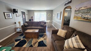 A living room with a brown sofa, a coffee table, and a rug. There is a dining area with a table and chairs in the background. - The Railroad Ranch - Station Five (Youngstown)