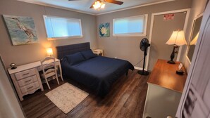A bedroom with a bed, bedside tables, a desk, a chair, a floor lamp, and a fan. - The Railroad Ranch - Station Five (Youngstown)