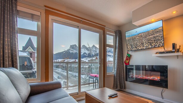 Un salon comprenant un canapé, une table basse, une cheminée et une grande fenêtre donnant sur une vue sur les montagnes.