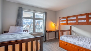 Une chambre avec deux lits, un bureau et une fenêtre donnant sur des immeubles et des montagnes.