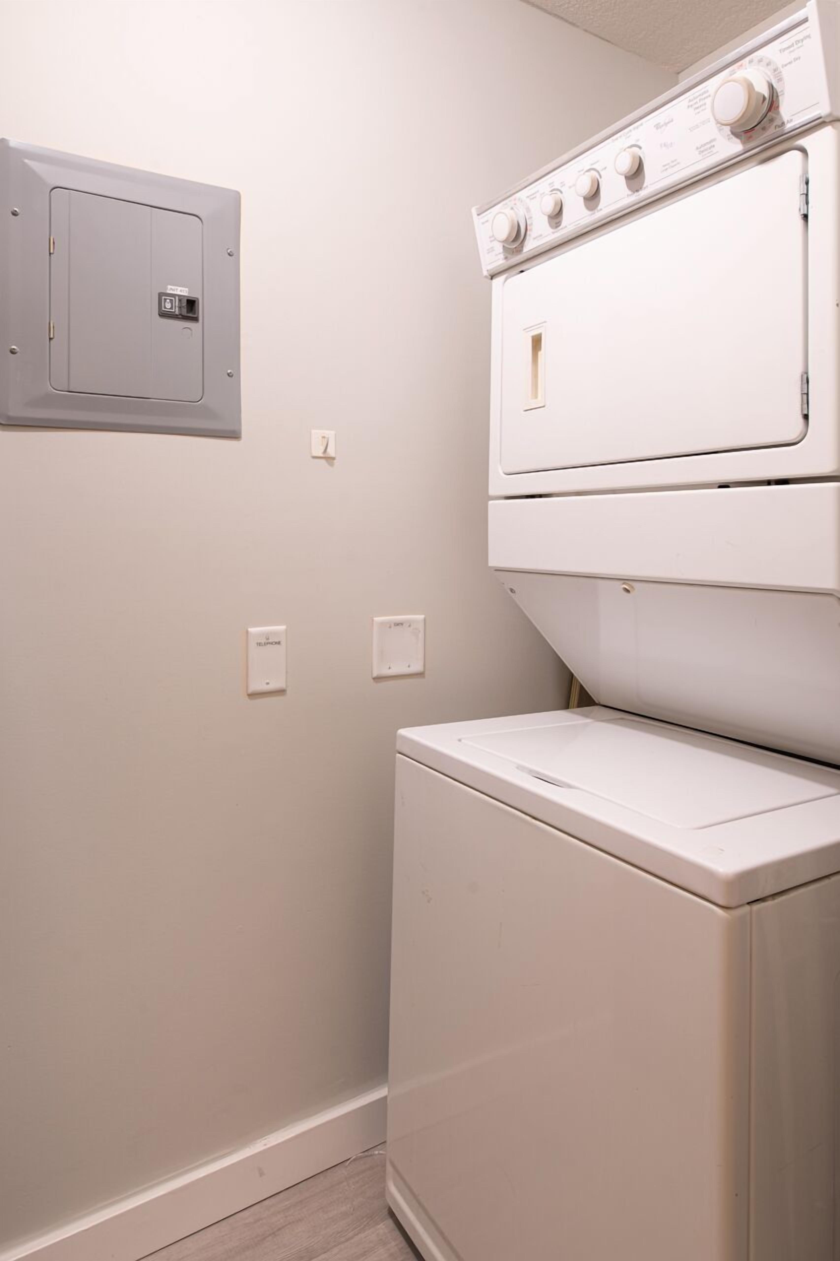 Ein Waschraum mit Waschmaschine und Trockner, einem Stromzähler und einem Thermostat an der Wand.