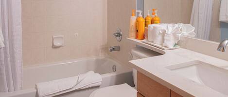 A bathroom with a bathtub, toilet, and vanity with toiletries.