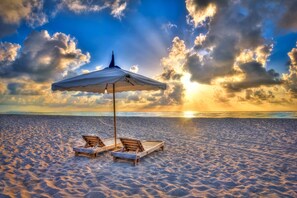 En strand med två träsolstolar och ett vitt parasoll under en klar himmel.