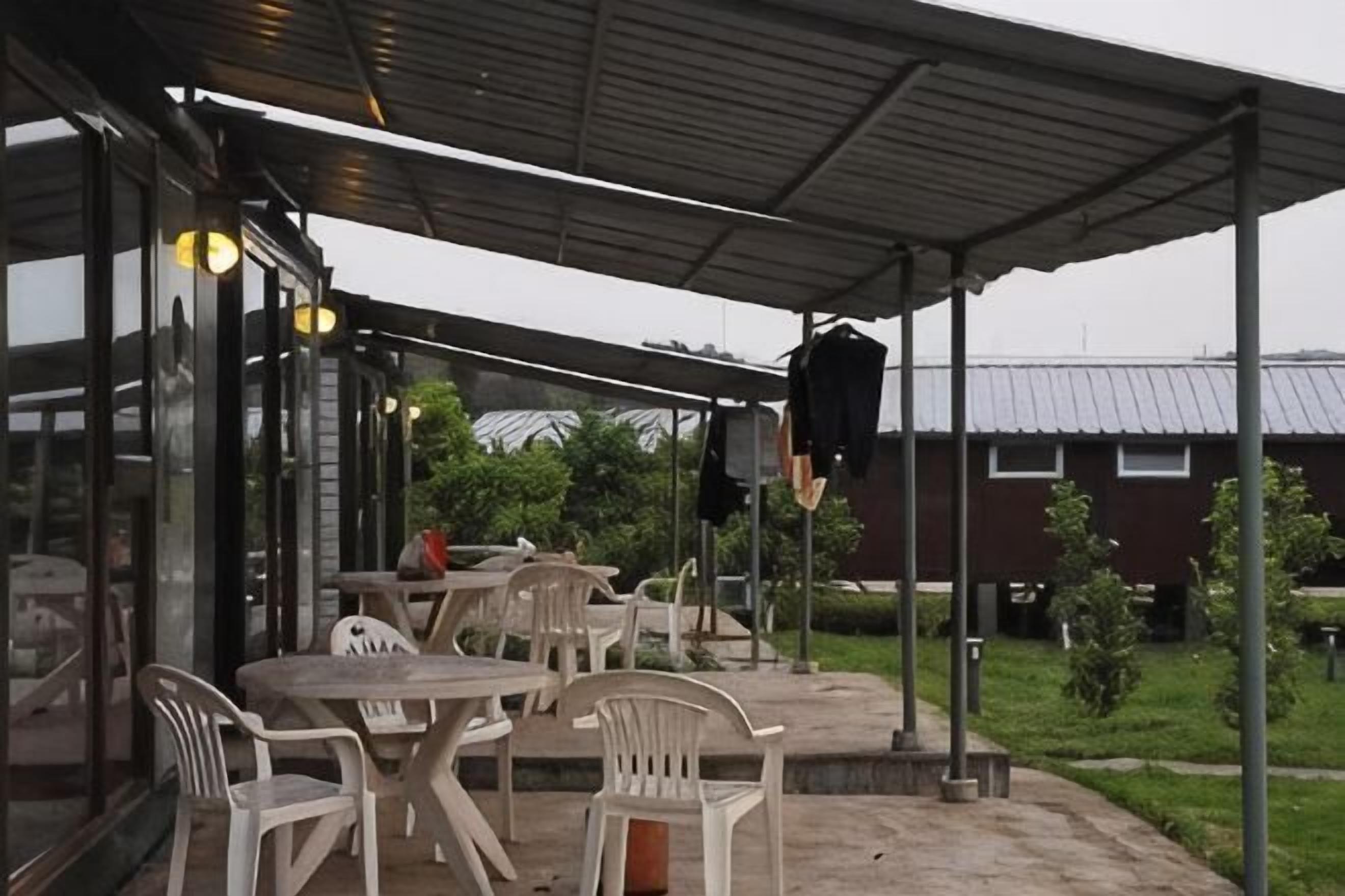 An outdoor patio with tables and chairs, a covered area, and a building with a metal roof in the background.
