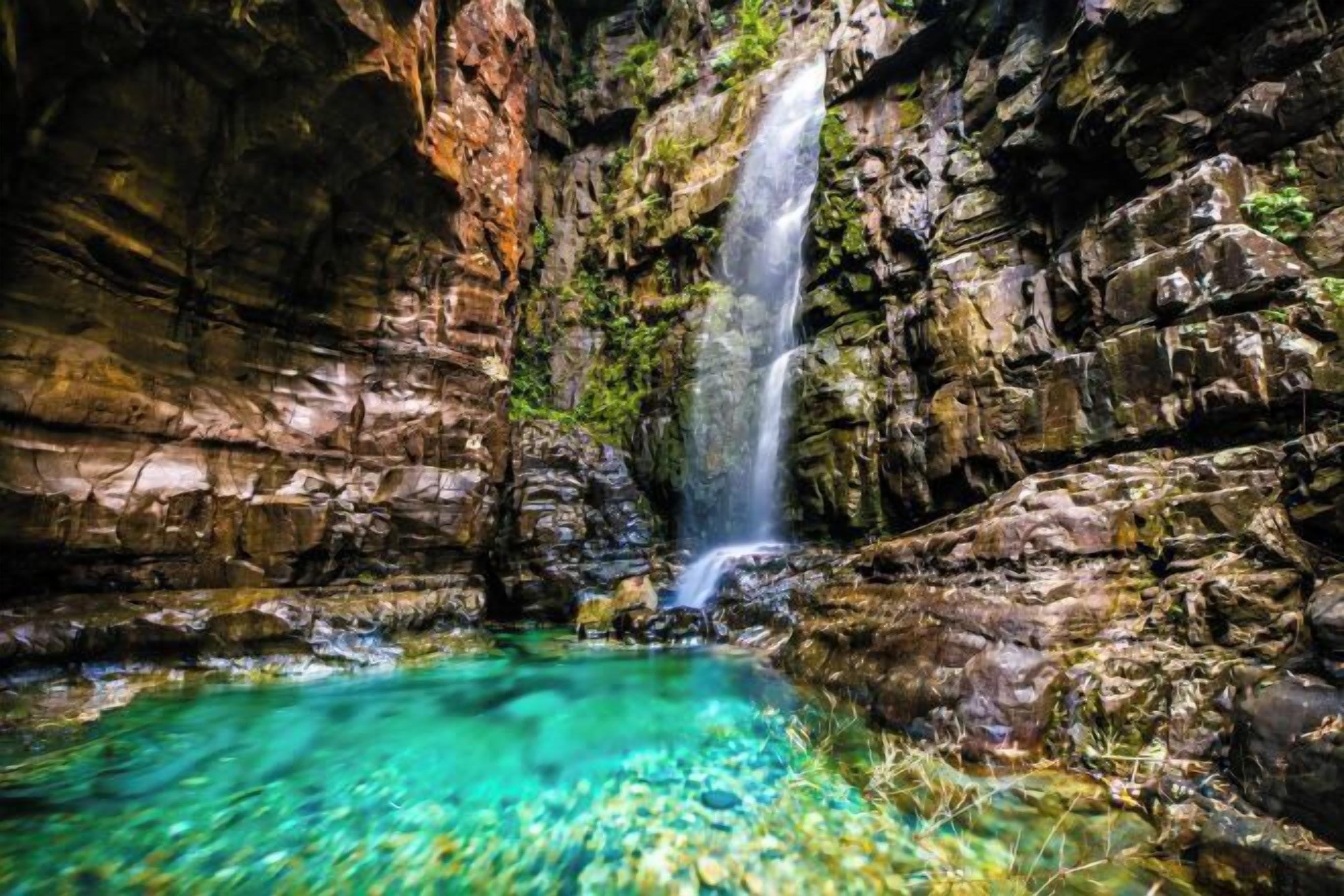 Formación rocosa natural con una piscina de agua clara y una cascada.